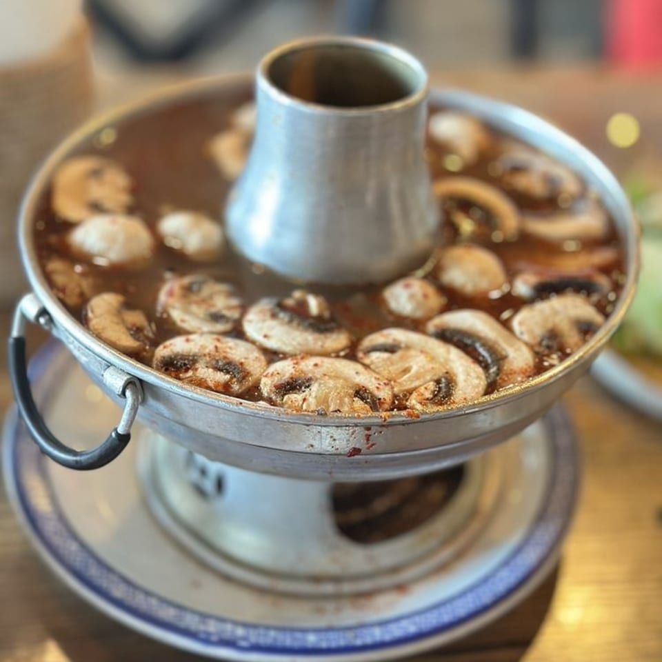 A metal hot pot filled with a dark broth and sliced mushrooms, ready to be served.