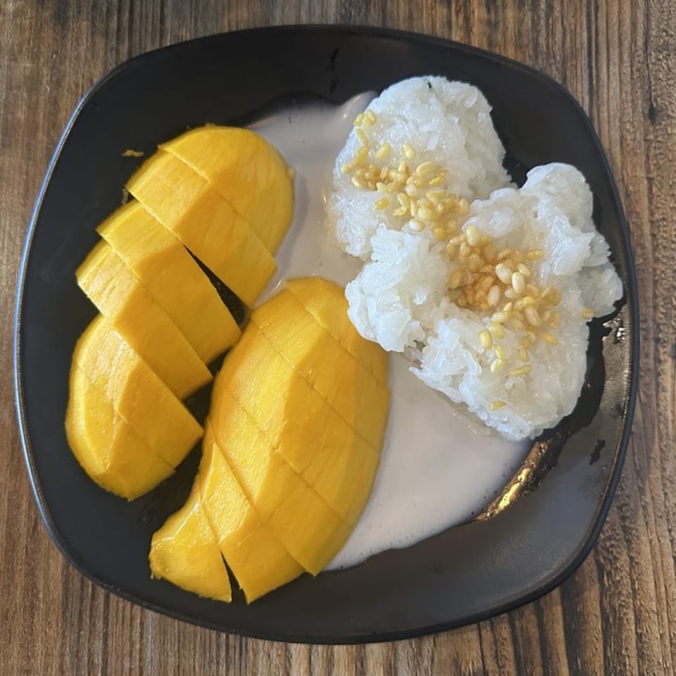 Mango sticky rice with coconut milk and sesame seeds on a black plate.