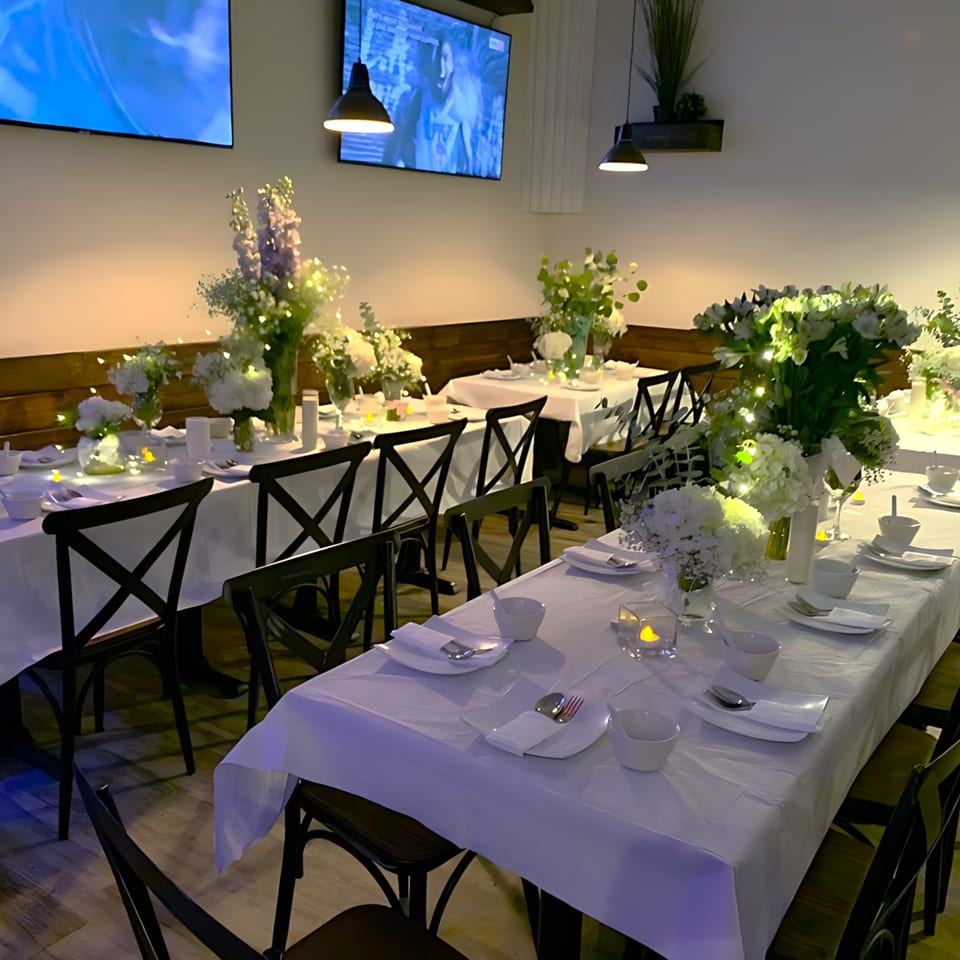 Elegantly set tables with white tablecloths, floral centerpieces, and black chairs in a restaurant dining room.