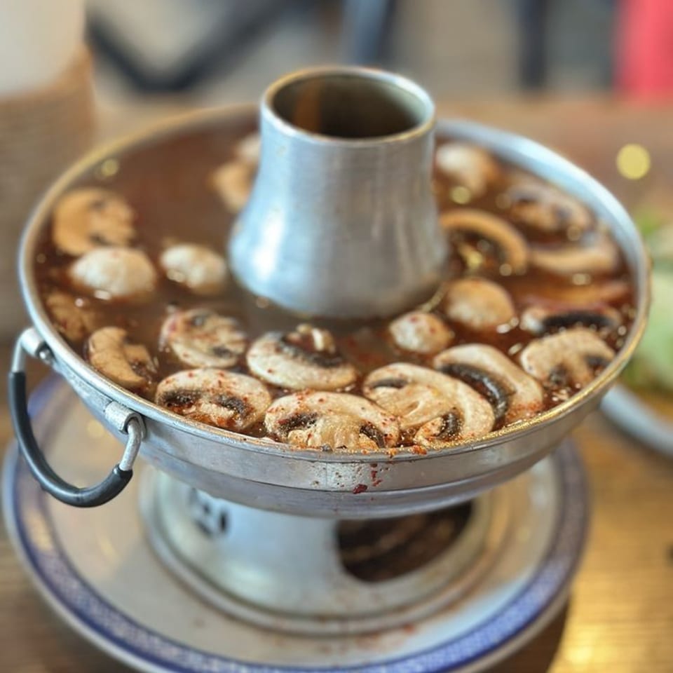 Thai hot pot with sliced mushrooms in a rich broth, served on a patterned plate.
