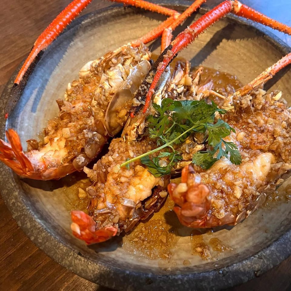 Three large, whole prawns with bright red legs, covered in garlic sauce and garnished with cilantro.