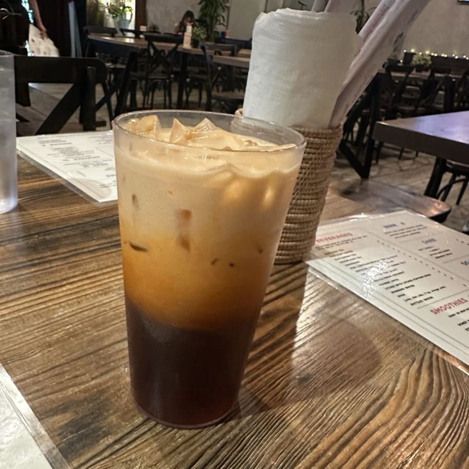 Iced Thai tea with a creamy top layer and dark bottom layer on a wooden table at Pattaya Bay.