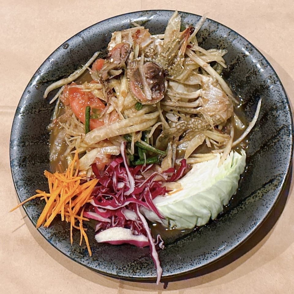 Som Tum Pu Pla Ra, a Thai papaya salad with crab, tomatoes, and green beans, served with cabbage.