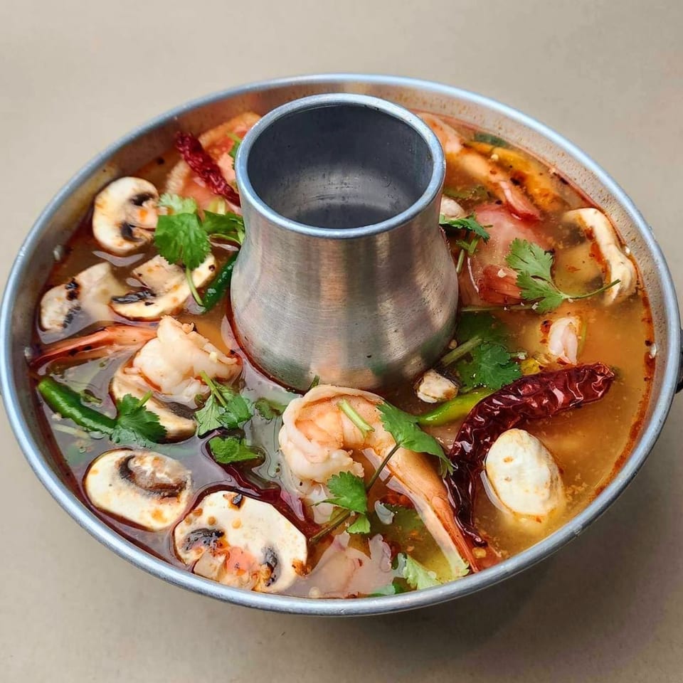 Spicy Tom Yum soup with shrimp, mushrooms, and herbs in a traditional Thai hot pot.