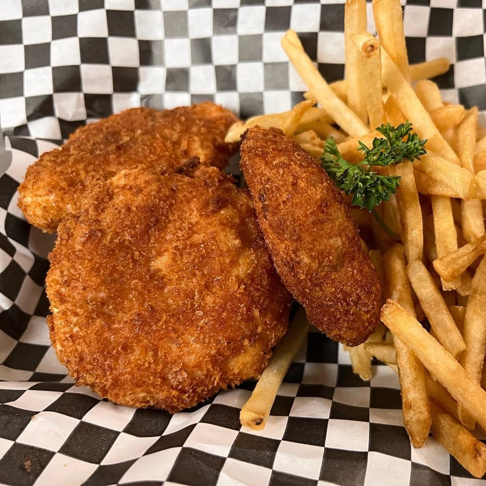 Crispy fried chicken pieces and golden french fries with a sprig of parsley on checkered paper.