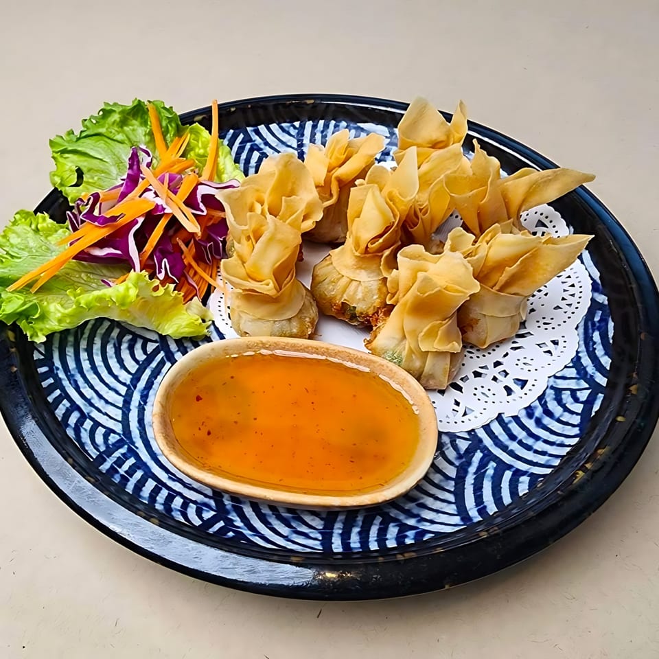 Golden fried Thai money bags with sweet chili sauce and a side salad on a blue and white plate.
