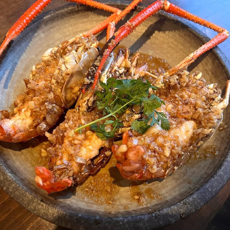 Three large, red-orange lobsters covered in garlic sauce and garnished with parsley in a dark bowl.