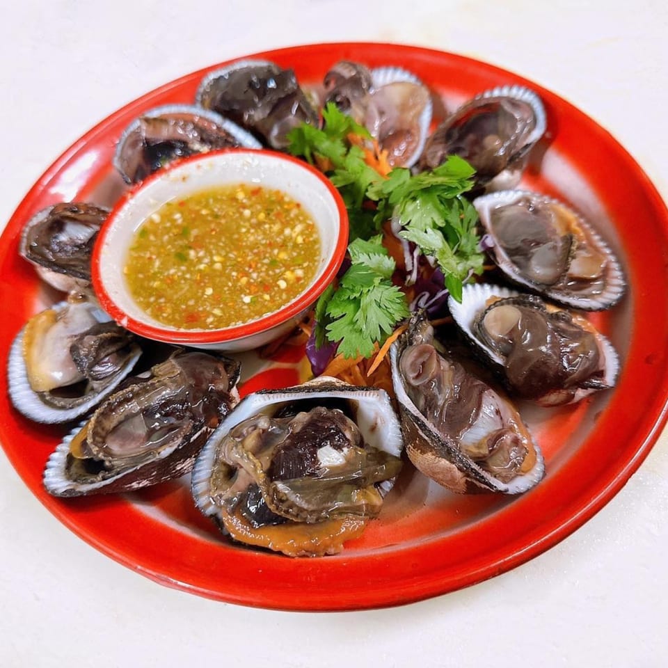 Fresh cockles on a red plate with a side of spicy Thai seafood dipping sauce.
