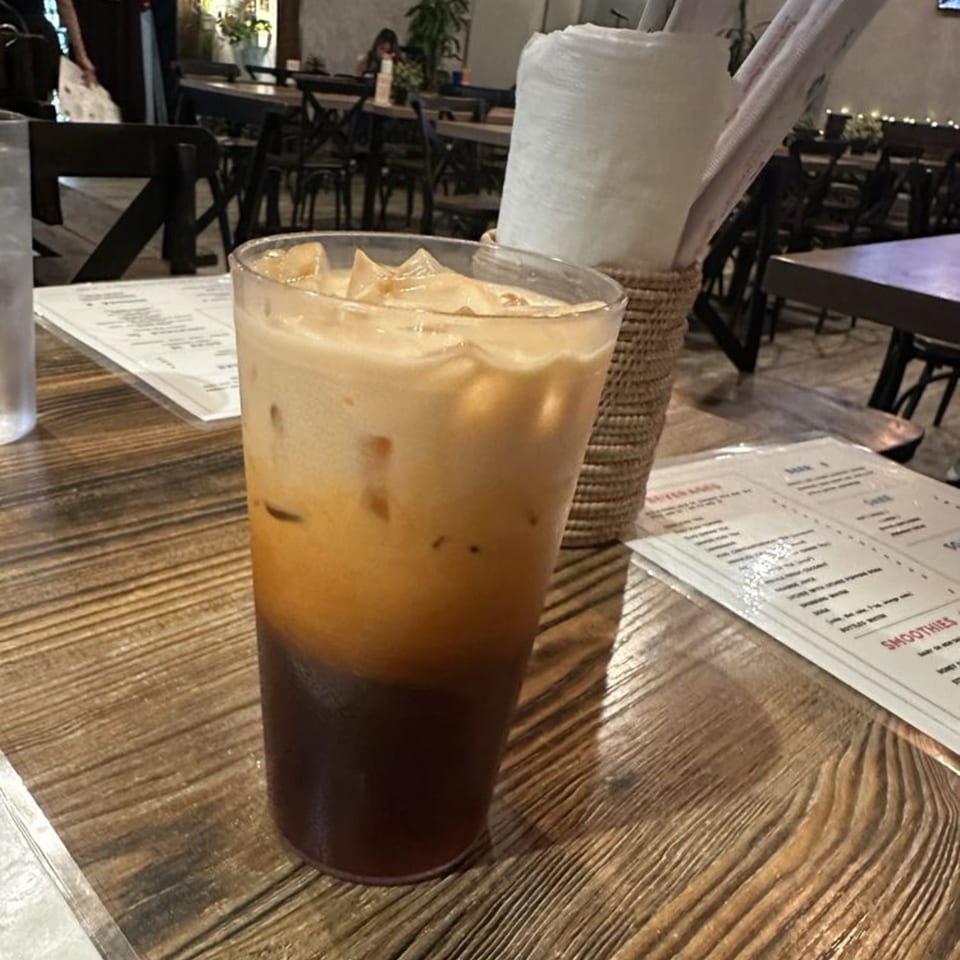 Iced Thai tea with a creamy top layer and dark bottom layer on a wooden table at Pattaya Bay.