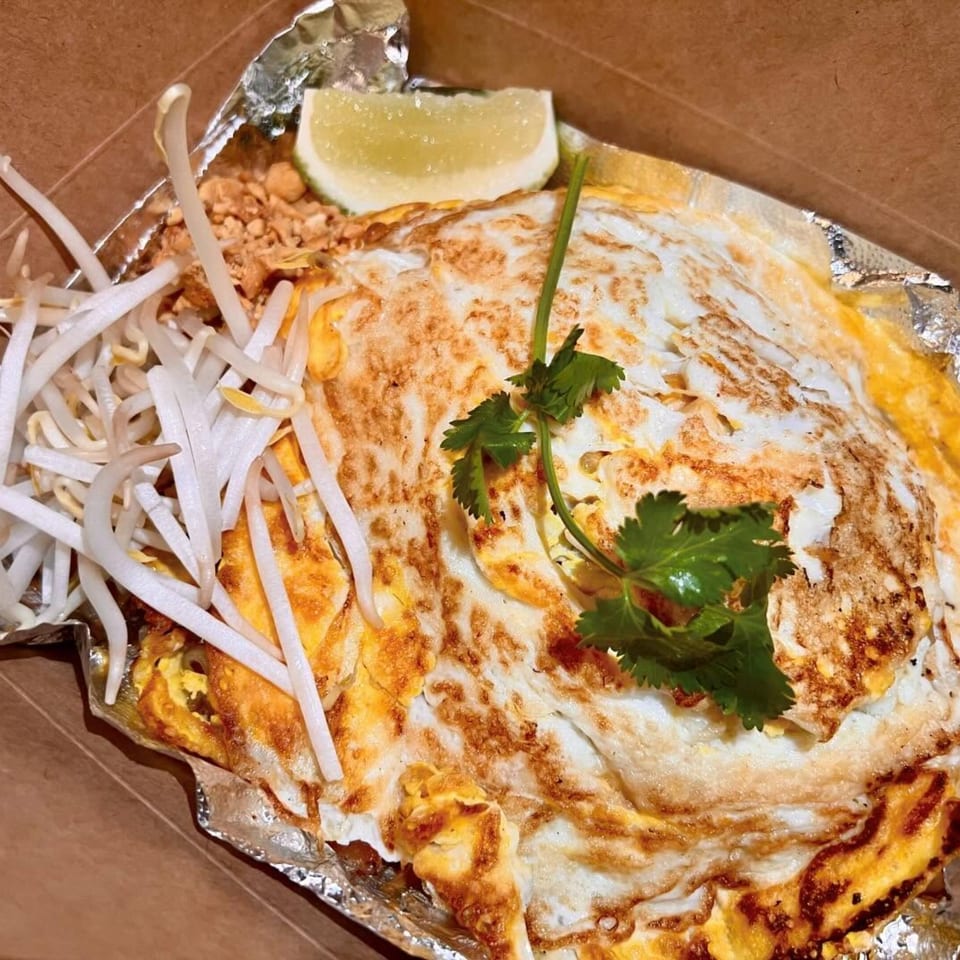 Thai Pad See Ew with fried egg, bean sprouts, cilantro, and lime in a takeout container.
